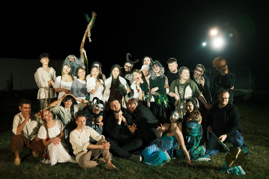 The cast of “Kwiat Paproci” by Teatr Muzyczny Druga Zwrotka posing in costume and make-up, outdoors at night.